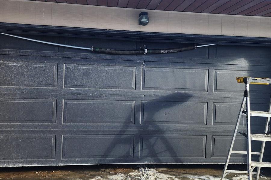 DPS Garage Doors repairing the torsion spring on a dark double garage door with a ladder set up in the GTA